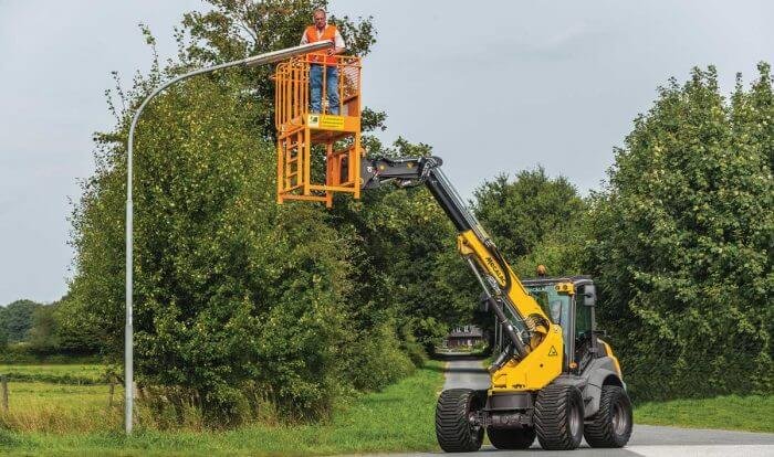 The photograph shows a telescopic loader supporting the worker on site.